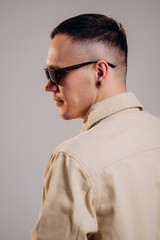 Fototapeta premium Stylish young man poses in a beige shirt and modern sunglasses. Men's accessories, optics. Studio portrait.