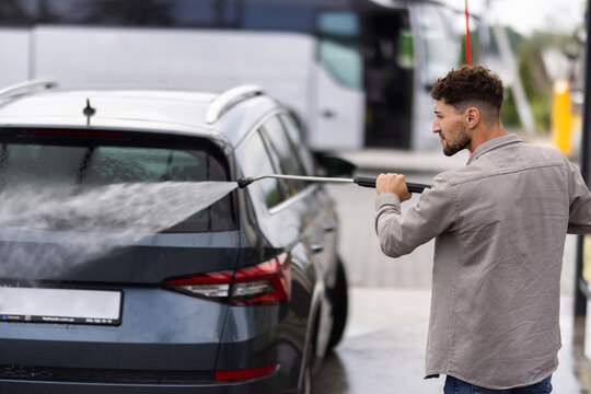 Young man washing his car under high pressure water outdoors