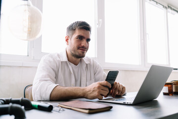 Naklejka na ściany i meble Smiling male entrepreneur using smartphone while working on computer
