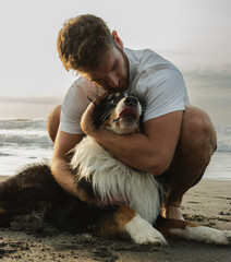 man gives a hug to his dog on the beach