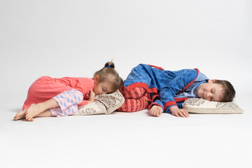 Two children - brother and sister in pajamas lie on pillows and pretend to be asleep