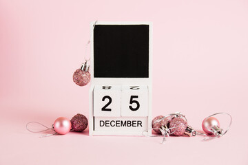 Christmas, wooden calendar with date December 25 and Christmas tree decorations on pink background. Christmas and New Year celebration concept.