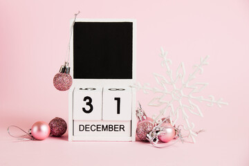 New Year, wooden calendar with the date December 31 and Christmas tree decorations on a pink...