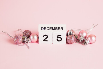 Christmas, wooden calendar with date December 25 and Christmas tree decorations on pink background. Christmas and New Year celebration concept.