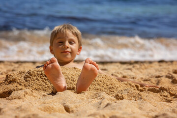 Child, tickling sibling on the beach on the feet with feather, kid cover in sand, smiling, laughing