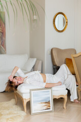 A woman is lying on a sofa in a stylish, bright living room next to a beautiful picture she painted herself.