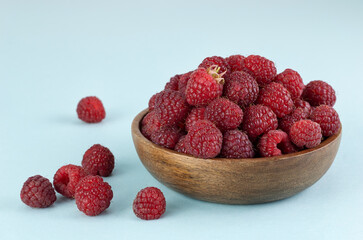 Fresh raspberries in a wooden bowl on a blue background.