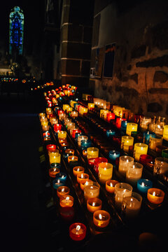 Fotografía en vertical de un conjunto de velas de colores encendidas dentro de una iglesia en Mont Saint Michel, Francia.