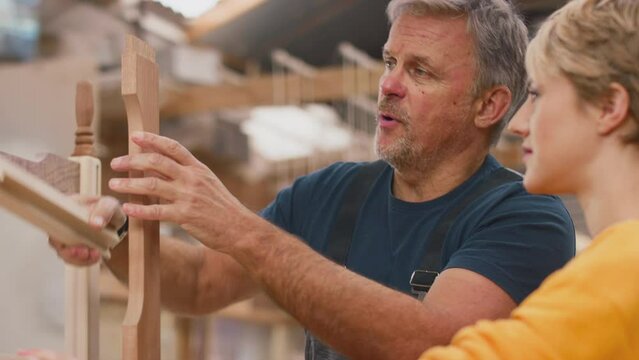 Mature male carpenter sharing woodworking skills with female apprentice in furniture factory - shot in slow motion
