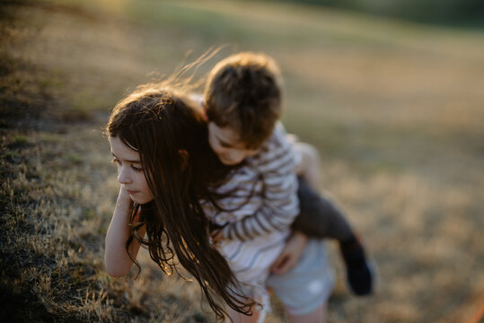 Abstract, blurred image of a sister giving her younger brother a piggyback ride in a field at sunset