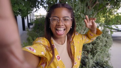 Cheerful young African American woman using smartphone on a video call, looking at camera and waving while being at university. Point of view of an student doing a selfie for social media. - Powered by Adobe