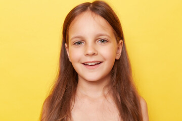 Naklejka premium Closeup portrait of smiling cheerful little girl with long hair standing isolated over yellow background being in good mood expressing positive emotions