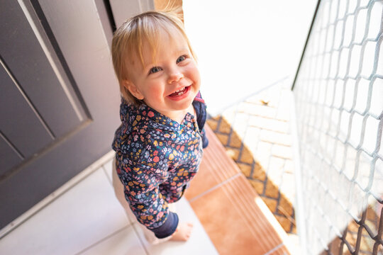 Toddler girl by front door step of house waiting to go outside for a walk with parent