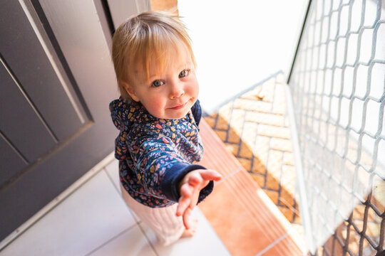 Toddler girl by front door step of house waiting to go outside for a walk with parent