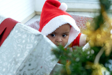 African baby girl wears Santa hat sitting in big Christmas present box near Christmas tree, happy new year and merry Christmas