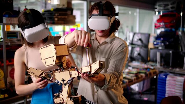 Two young engineers fixing a mechanical robot in the workshop, using VR virtual reality headsets