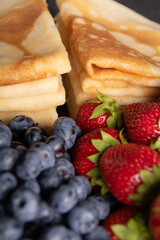 photo ripe, juicy berries blueberries and strawberries in the foreground in a blur, in the background thin pancakes stacked in a slide