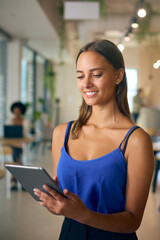 Young Businesswoman Standing In Busy Office Using Digital Tablet