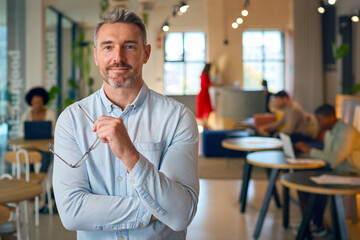 Obraz premium Portrait Of Smiling Mature Businessman Holding Glasses Standing In Busy Office 
