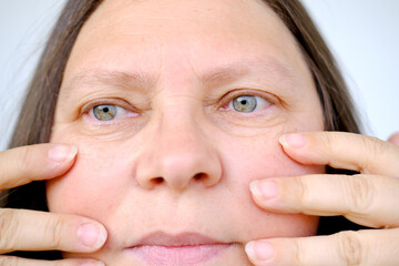 closeup female face woman 50 years old, looks in mirror, checks skin turgor, applies Hyaluronic...
