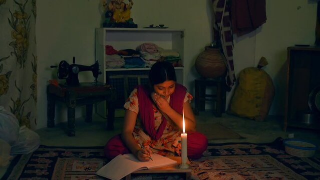 A village girl is sweating while studying under the candle - poor family  hard work  lack of electricity  poor infrastructure . A teenage girl completing her homework in dark - village education  r...