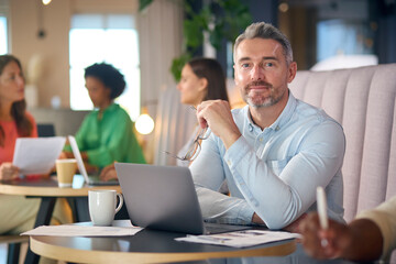 Portrait Of Mature Businessman Working On Laptop In Informal Seating Area Of Modern Office