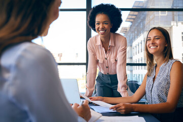 Female Multi-Cultural Business Team Meet Around Boardroom Table With Laptops Discussing Documents