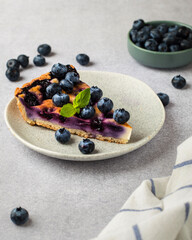 a plate with a piece of blueberry pie, in the background berries in a bowl, on a light.