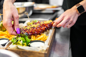 woman chef hands cooking Grilled smoked pork ribs with french fries, onion rings, vegetables and sauce on kitchen