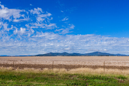 Blue autumn sky over dry stubble paddock on country farm with distant mountains on horizon