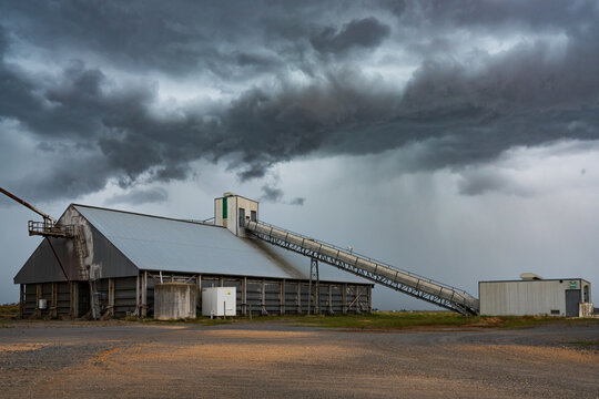 Rain falling from a dramatic stormfront over a grain storage shed in a rural setting