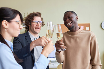 Portrait of three colleagues clinking champagne glasses in office and laughing happily during office party