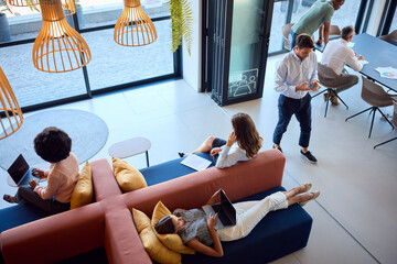 Overhead View Of Modern Open Plan Office With Staff Working Around Table And Breakout Seating Area