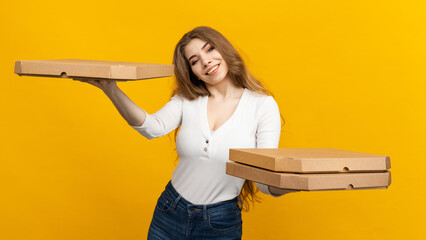An attractive woman holds pizza boxes on a yellow background in two hands. Ordering food for a large company. Fast food