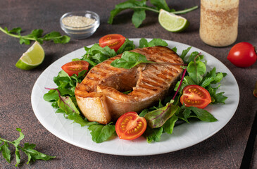 Baked salmon steak served with arugula and cherry tomatoes on a white plate