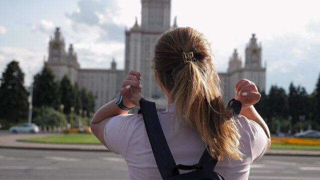A view from the back of a female student with a backpack on her back, she stands and looks at the large building of the state University. The first day of college. Moscow State University.