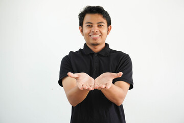 smiling young asian man posing on a white backdrop holding something with palms, offering to camera, wearing black polo t shirt.