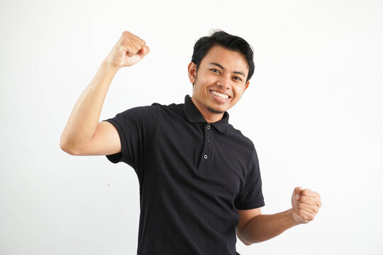 Smiling Or Happy Young Asian Man Clenched His Fists Cheering Carefree And Excited. Victory Concept, Wearing Black Polo T Shirt Isolated On White Background