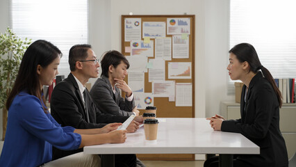 asian female job applicant entering and sitting opposite to a company recruiter hr team of three. she answers questions with hand gestures at the interview