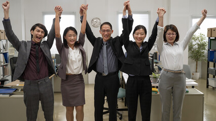 portrait of happy business team of five holding and raising their hands up while looking at camera cheering for teamwork success