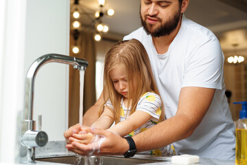 Father and daughter washing their hands above the sink in a kitchen
