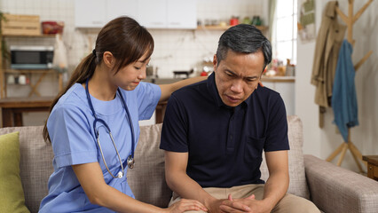 Asian female psychotherapist giving mental support to depressed elderly male patient. She taps his...