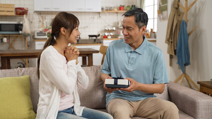 smiling asian daughter giving happy father a surprise present for Father’s Day celebration at home. she removes hand from his eyes and hopes he likes the gift