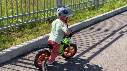 toddler child riding balance bike in parking lot in summer