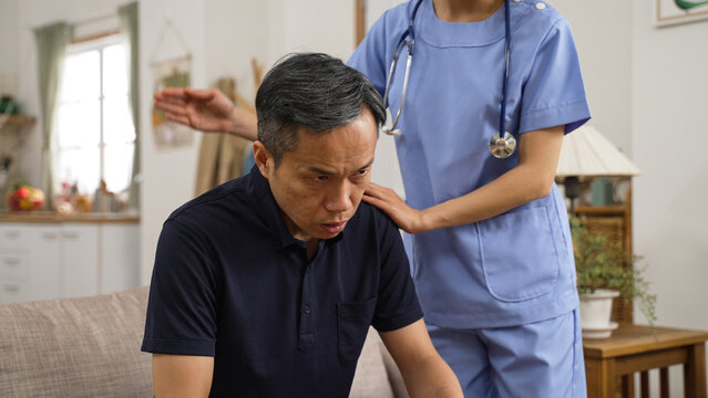 closeup of asian senior man is coughing while home attendant is patting on his back to help loose the sputum from lung in living room at home. domiciliary care concept