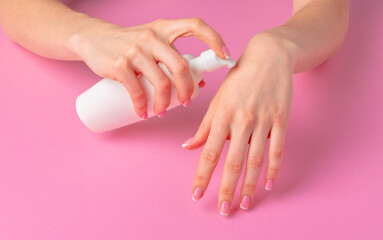 Female hand holding skincare product bottle on pink
