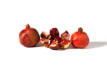 Three pomegranate fruits are depicted on a white background, one of which is broken into pieces.