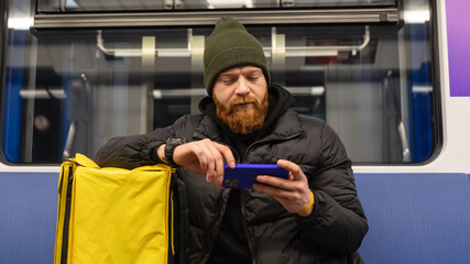 A male courier watches movies on his phone while riding the subway for an order. Metro is the fastest form of public transport
