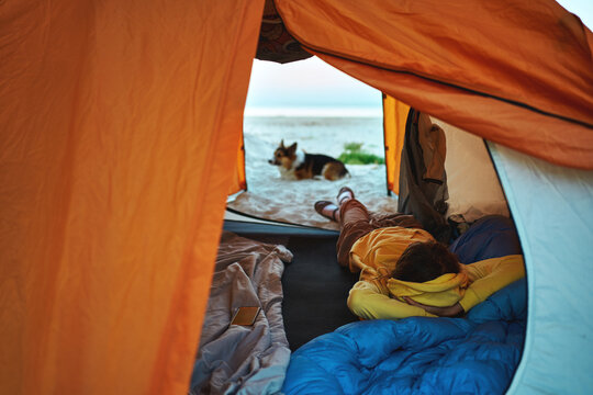 Perfect getaway as a woman tourist lies comfortably in a tent, overlooking a tranquil beach with her adorable Corgi pet companion by her side