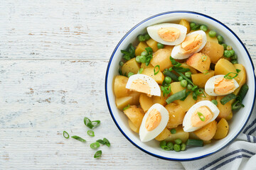 Traditional Potato salad with bacon and eggs in a white bowl. Picnic food concept. Bowl of warm potato salad. German Kartoffelsalat. Top view.